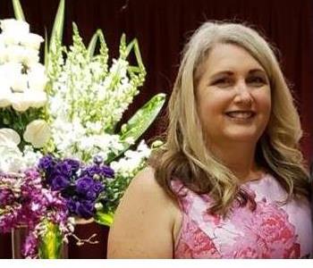 female manager with blonde hair smiling in front of flowers